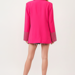 Model wearing hot pink embellished blazer with white tank and denim shorts - back view