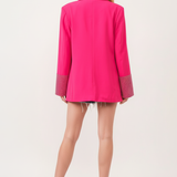 Model wearing hot pink embellished blazer with white tank and denim shorts - back view